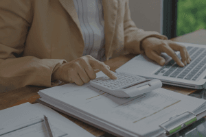 Close-up of someone using a calculator and laptop to review financial documents, representing fund accounting for charities and nonprofits.